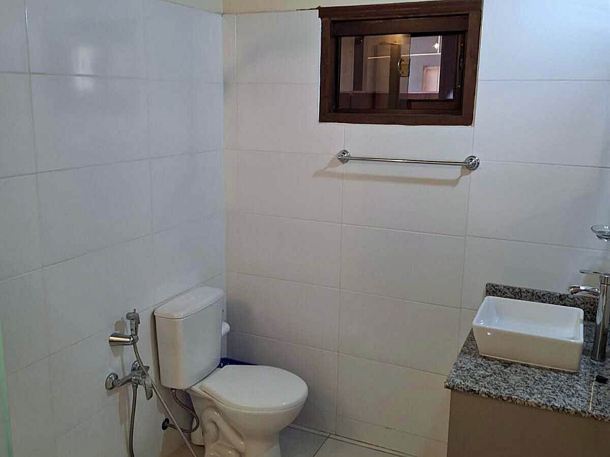 Helles Bad in Paraguay mit weißen Fliesen, Toilette, eckigem Waschbecken auf Granit und kleinem Holzfenster.