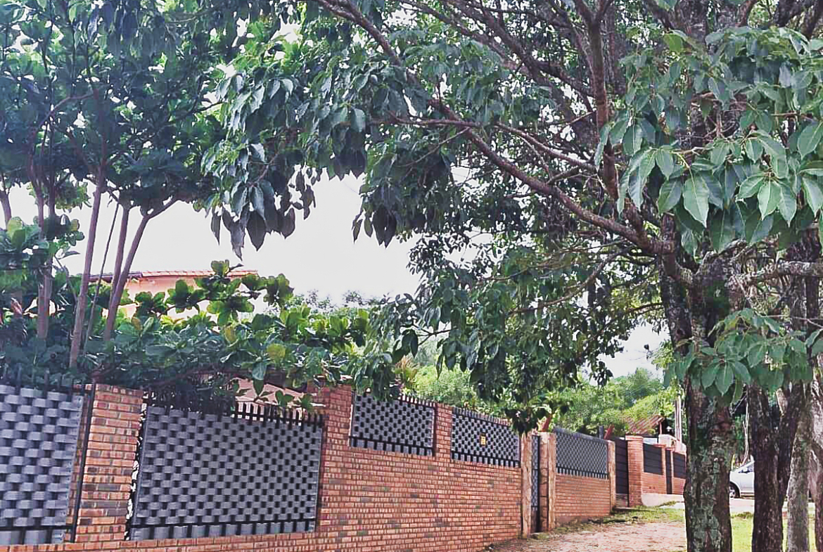 Paraguay Immobilie: Eine eindrucksvolle Ziegelmauer mit Metallzäunen und Bäumen schützt ein Grundstück in Paraguay.