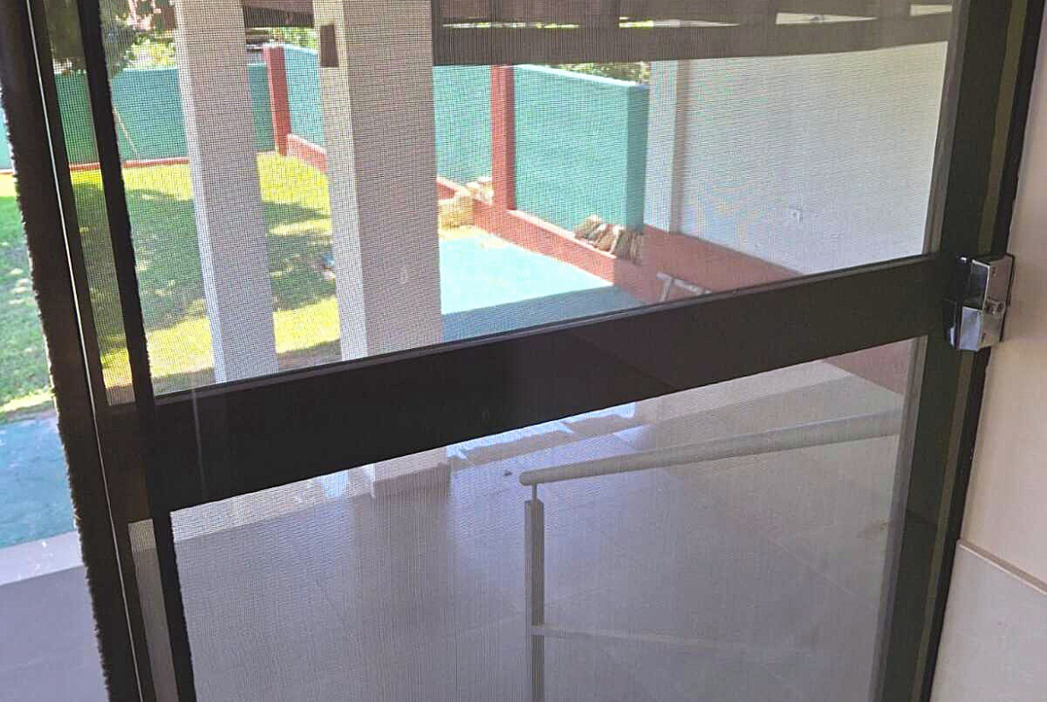 Blick durch ein Fliegengitter auf den sonnigen Gartenbereich einer Immobilie in Paraguay.
