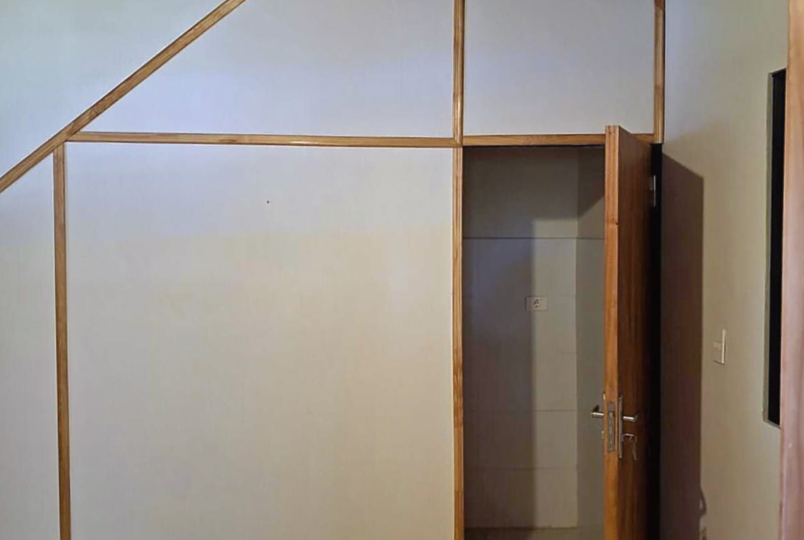 Detailansicht einer Immobilie in Paraguay mit weißer Wandverkleidung, Holzleisten und offener Holztür zu einem Nebenraum.