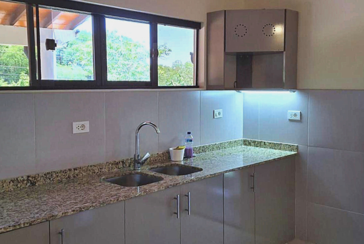 Moderne Küche in Paraguay mit Granitarbeitsplatte, Doppelspüle und Blick ins Grüne aus dem Fenster.