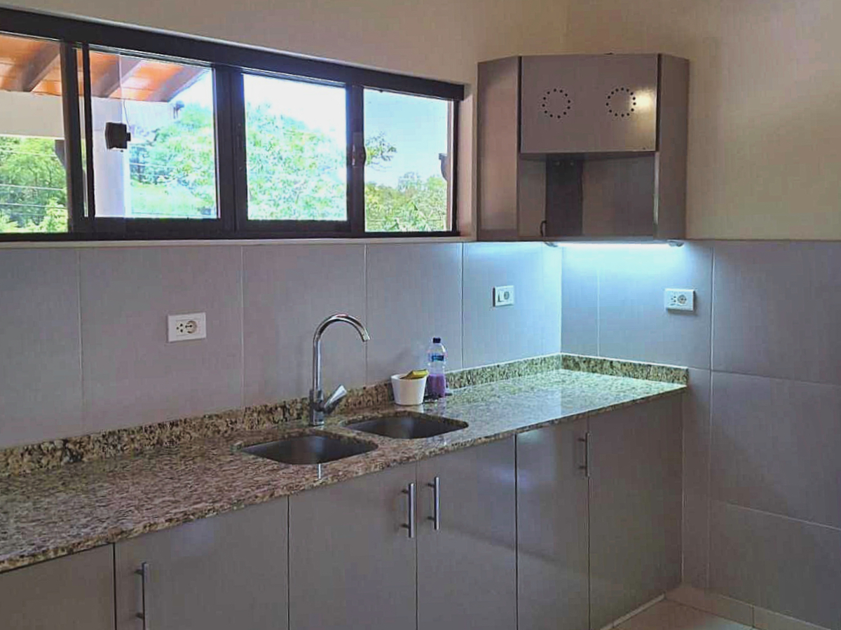 Moderne Küche in Paraguay mit Granitarbeitsplatte, Doppelspüle und Blick ins Grüne aus dem Fenster.