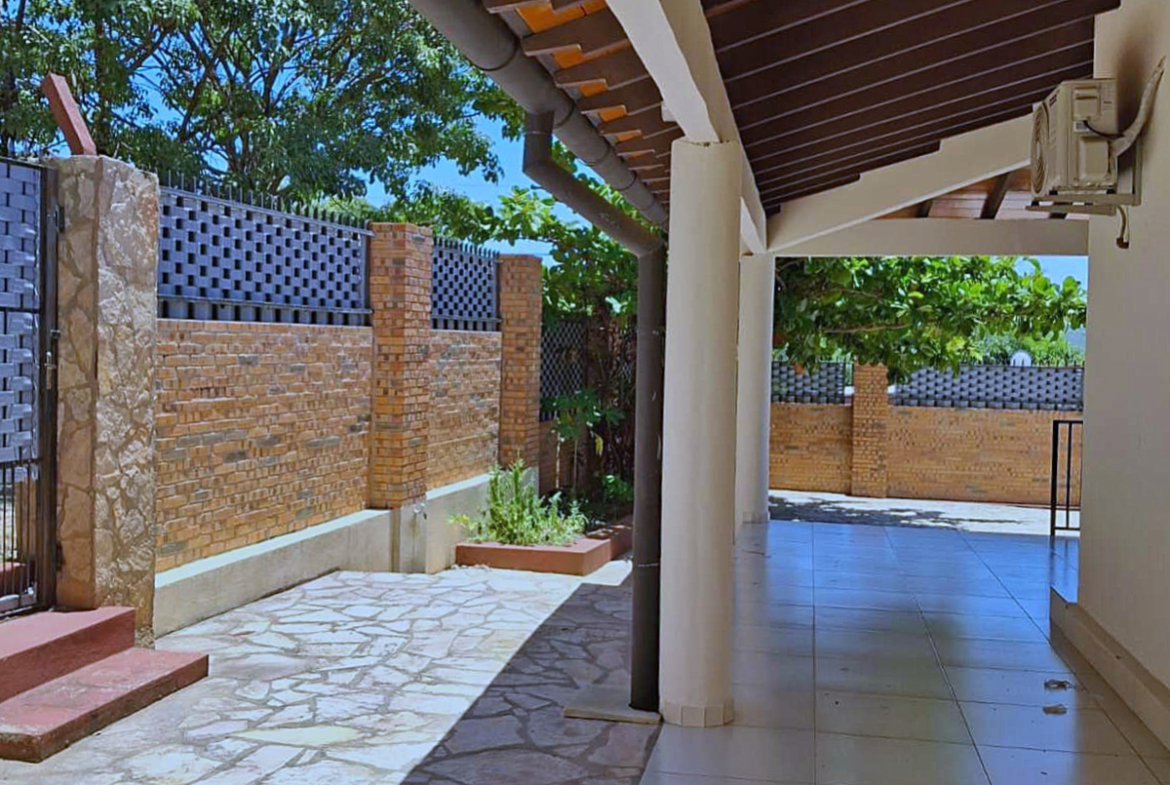 Einladender Außenbereich eines Hauses in Paraguay mit überdachter Terrasse, Ziegelmauer und gepflastertem Hof.