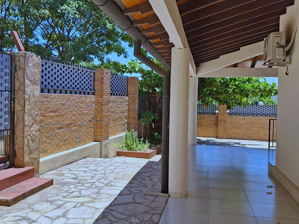 Einladender Außenbereich eines Hauses in Paraguay mit überdachter Terrasse, Ziegelmauer und gepflastertem Hof.