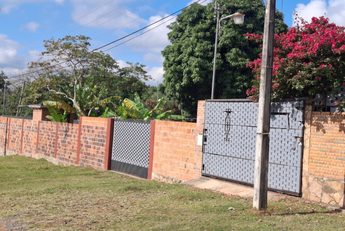 Immobilien Paraguay: Grundstück mit Ziegelmauer, zwei Toren und üppiger tropischer Begrünung unter blauem Himmel.